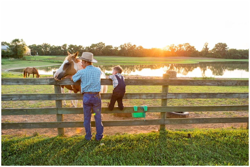 Dad and son standing at a horse paddock fence and watching the sun go down over the hills.